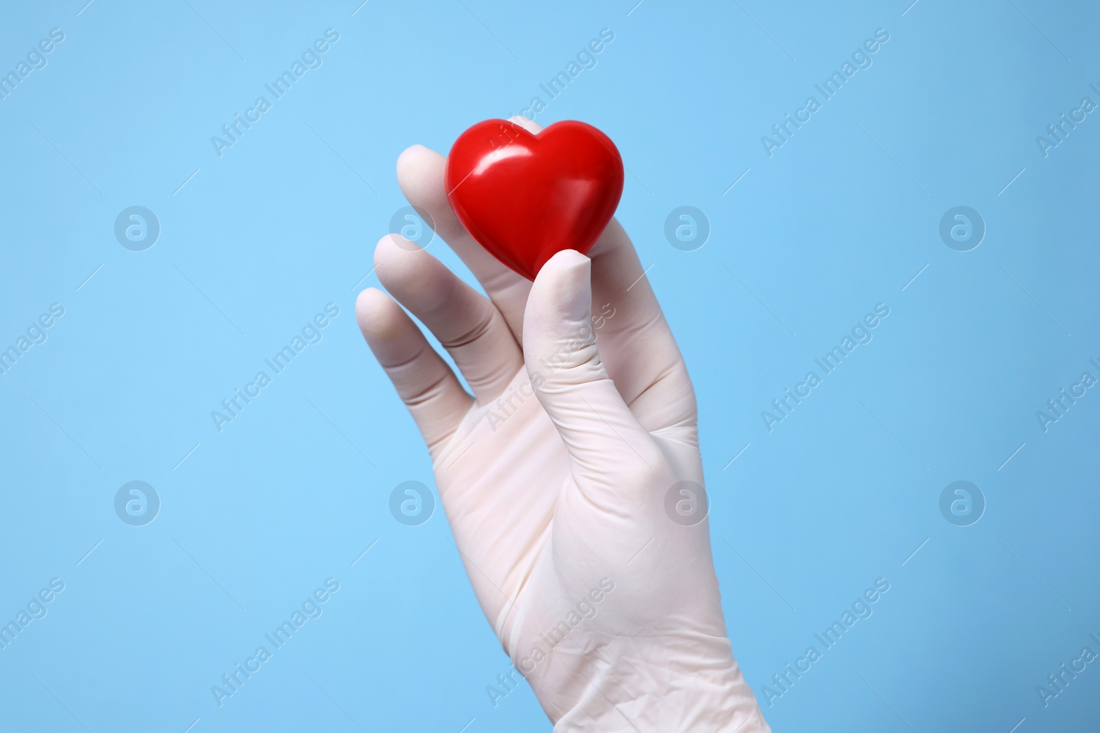 Photo of Doctor wearing white medical glove holding decorative heart on light blue background, closeup