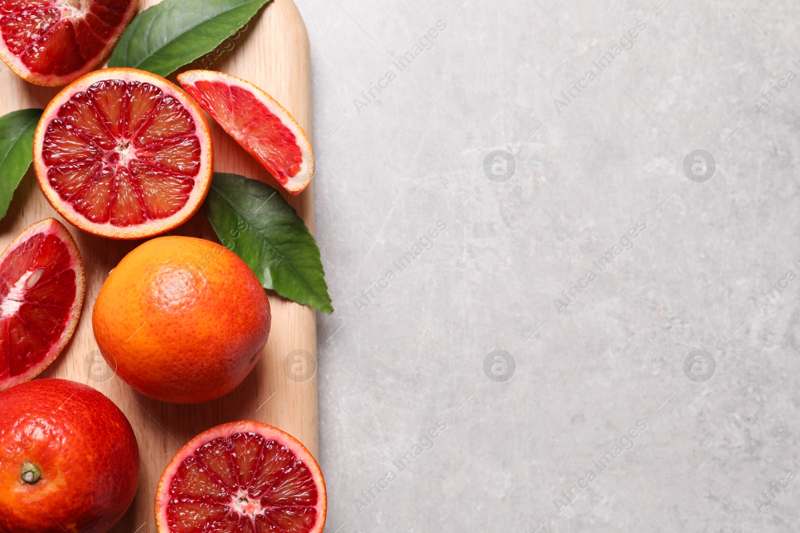 Photo of Ripe red oranges, green leaves and wooden board on light table, top view. Space for text