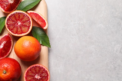 Photo of Ripe red oranges, green leaves and wooden board on light table, top view. Space for text