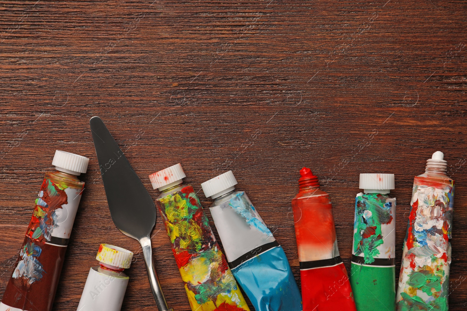Photo of Tubes with oil paints and spatula on wooden table, flat lay. Space for text