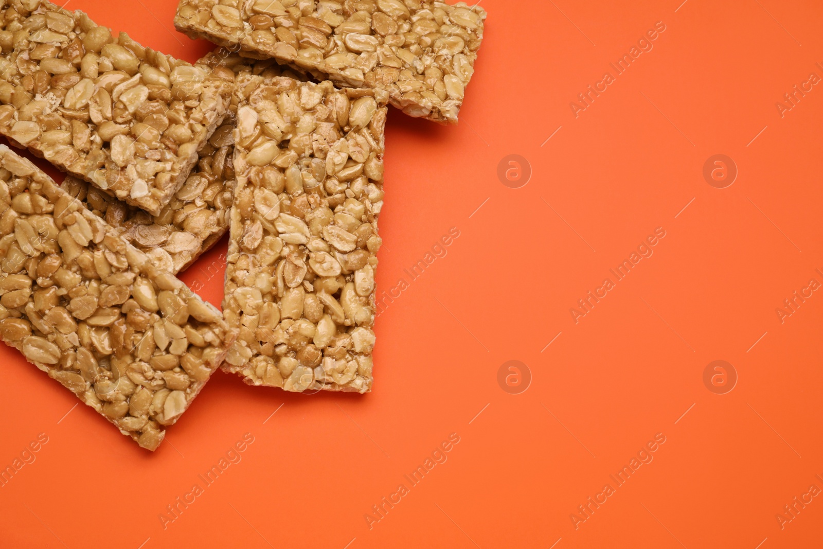 Photo of Tasty peanut bars (kozinaki) on orange background, flat lay. Space for text