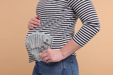 Photo of Surrogate mother. Pregnant woman with dollar banknotes on beige background, closeup