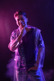 Photo of Young man wearing clear coat in neon lights with smoke effect