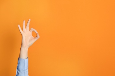 Photo of Young woman showing OK gesture on color background. Space for text