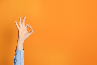 Young woman showing OK gesture on color background. Space for text