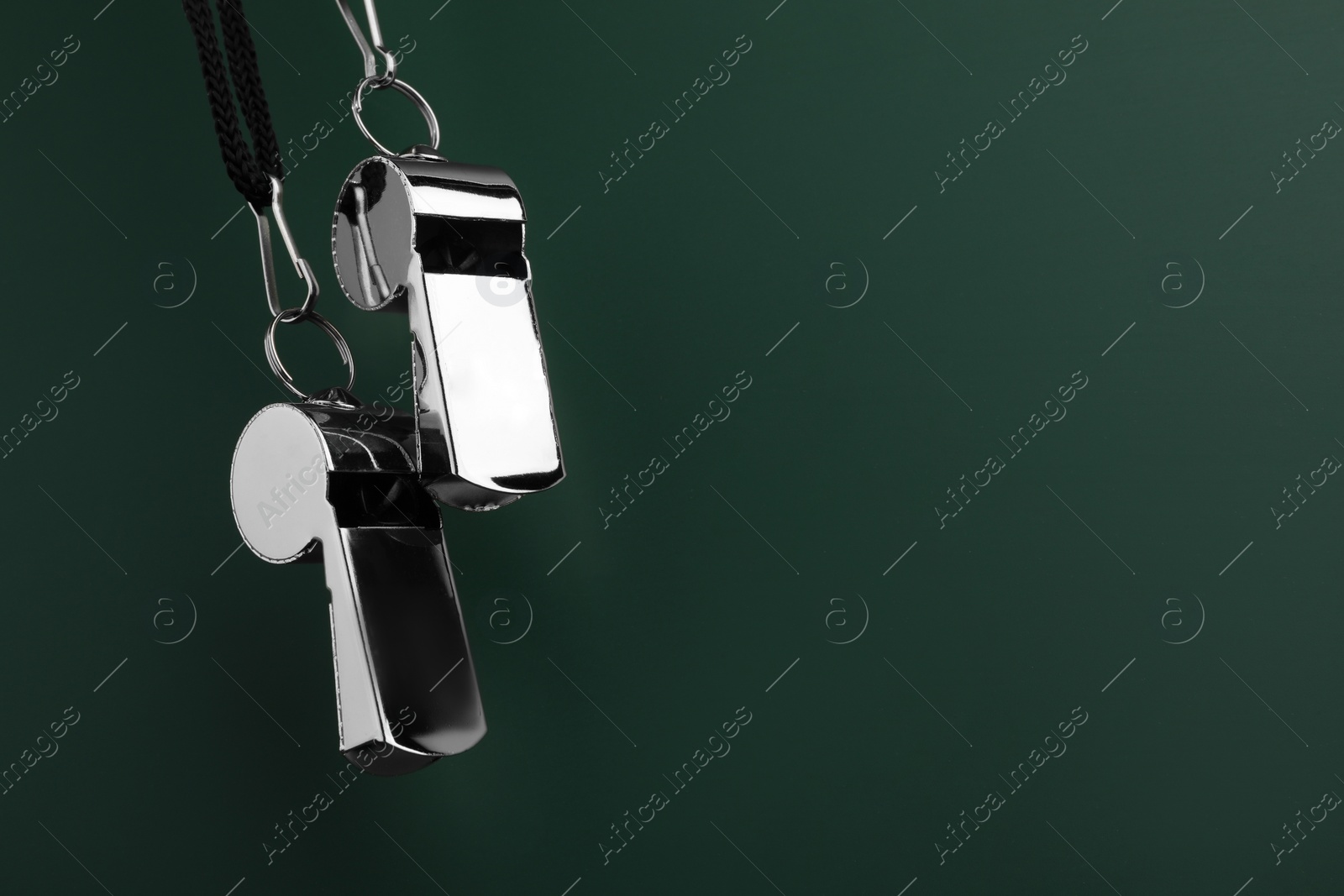 Photo of Referee equipment. Metal whistles on dark green background, closeup and space for text