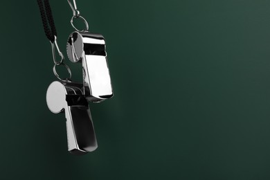 Referee equipment. Metal whistles on dark green background, closeup and space for text