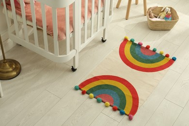 Stylish rug with rainbow on floor in baby room, above view