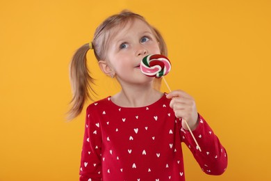 Photo of Portrait of cute girl licking lollipop on orange background