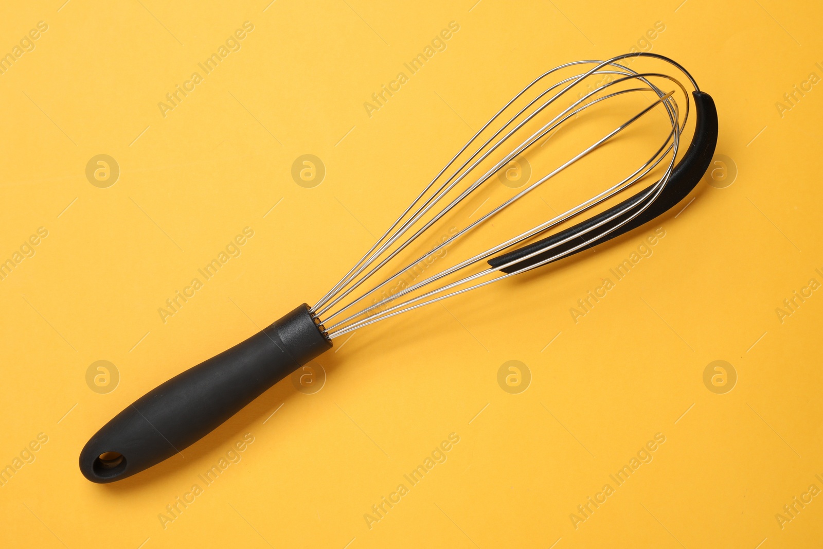 Photo of Metal whisk on yellow background, top view. Kitchen tool