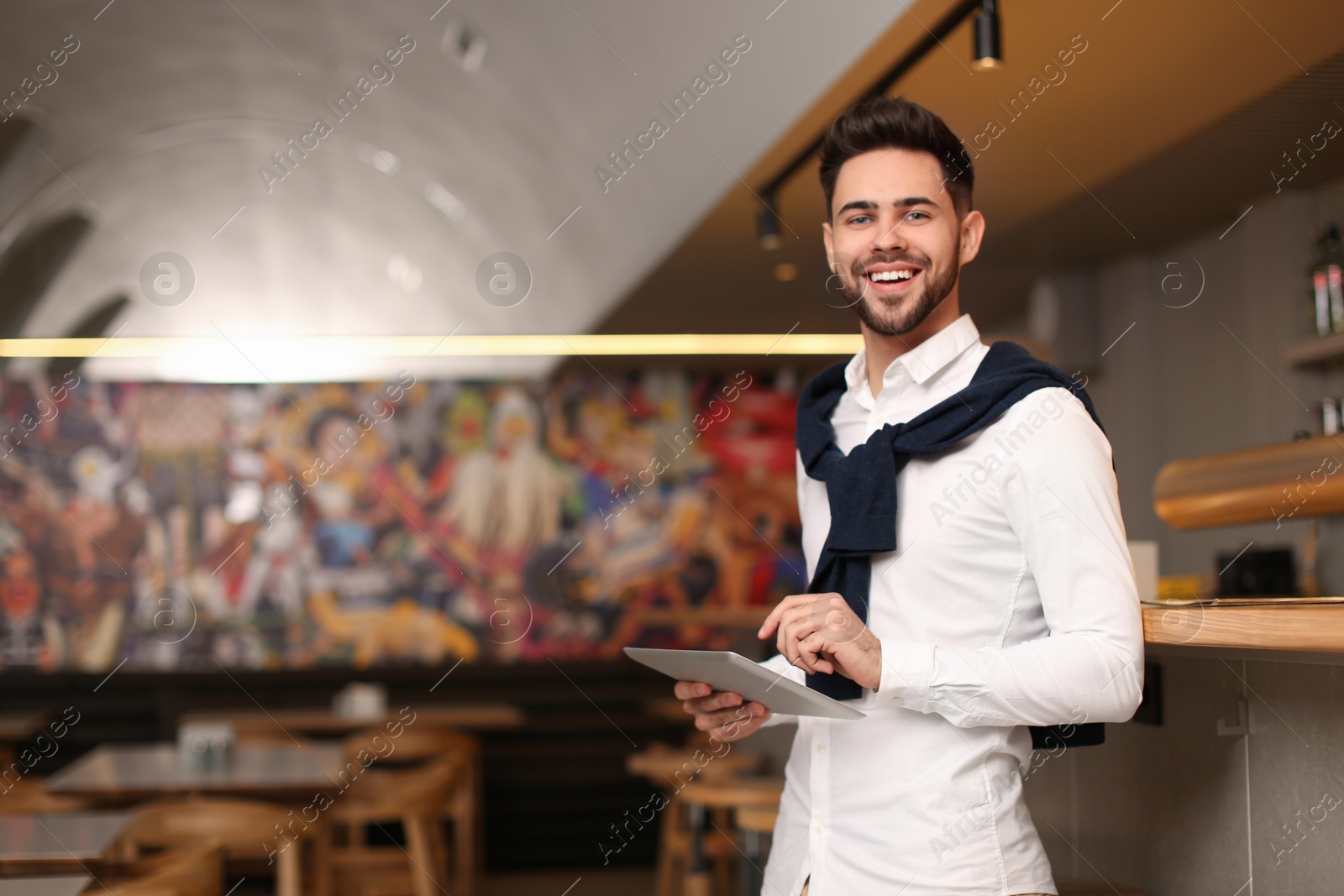 Photo of Young male business owner with tablet near counter in his cafe. Space for text