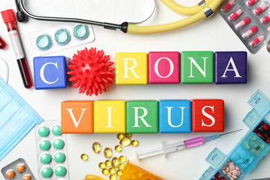 Photo of Cubes with phrase CORONA VIRUS and medicines on white background, flat lay