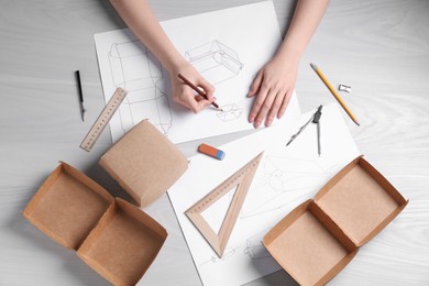 Woman creating packaging design at light wooden table, top view