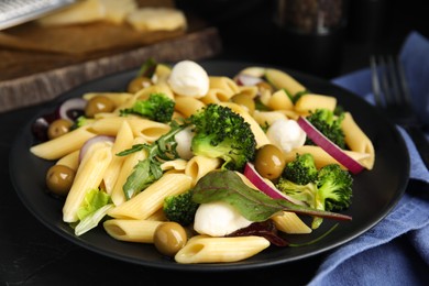 Photo of Plate of delicious pasta with broccoli, onion and olives on black table, closeup