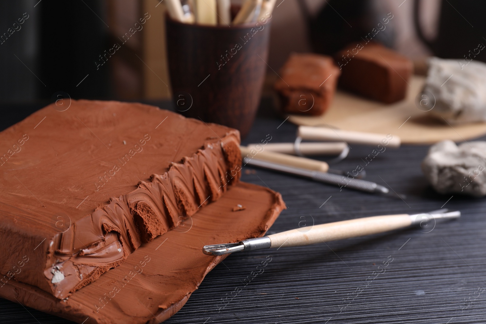 Photo of Clay and modeling tool on dark gray wooden table in workshop, closeup