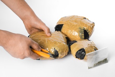 Photo of Smuggling and drug trafficking. Man opening package of narcotics with box cutter on white background, closeup