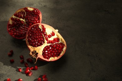 Photo of Pieces of ripe juicy red pomegranate with grains on grey textured table, space for text