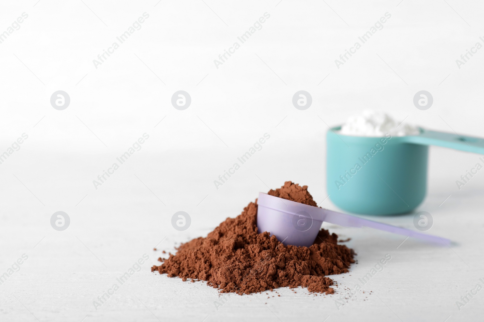 Photo of Scoops of different protein powders on white table, space for text