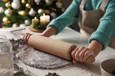 Photo of Little child rolling dough for Christmas cookies at white wooden table indoors, closeup