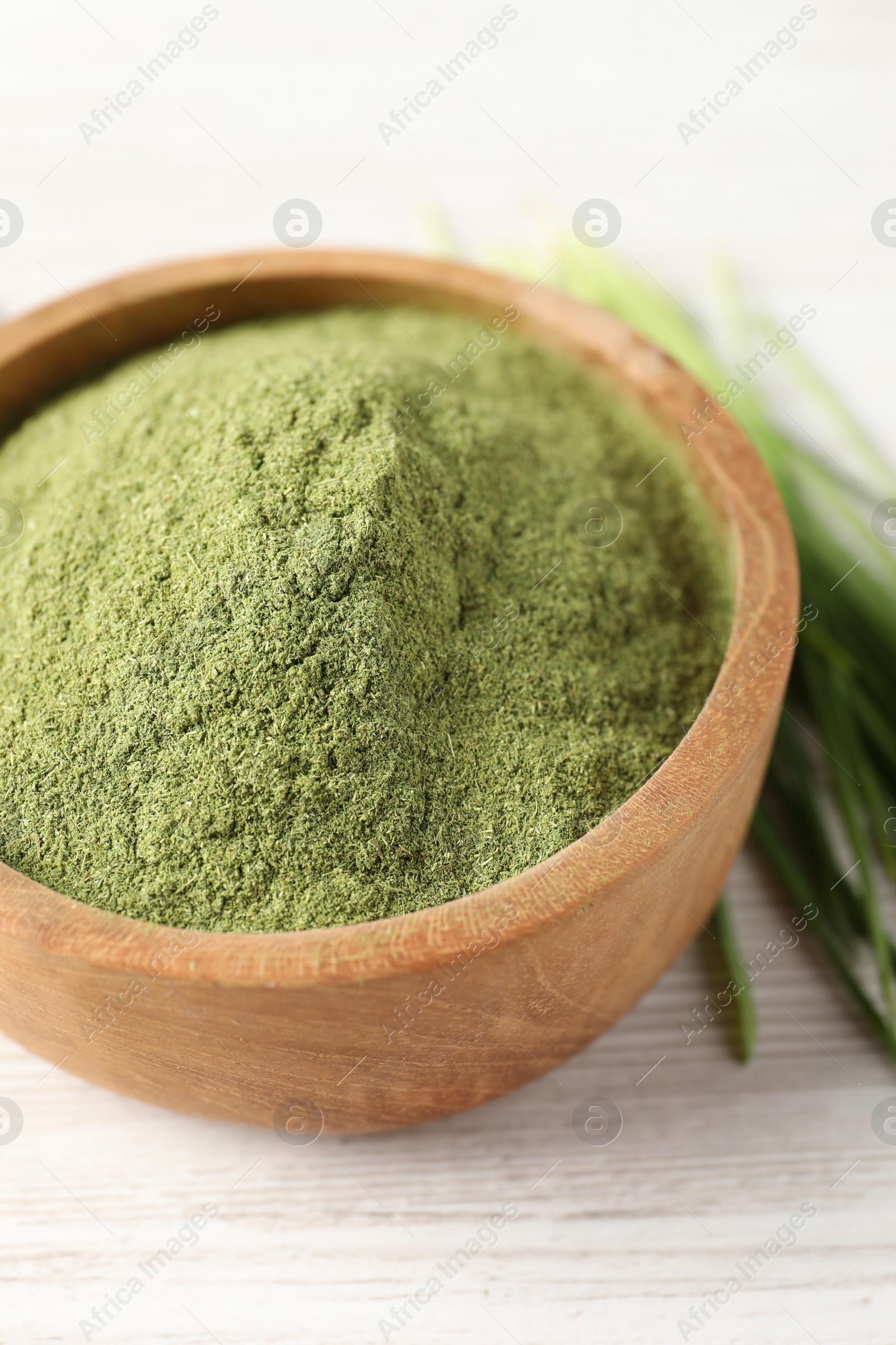 Photo of Wheat grass powder in bowl on white wooden table, closeup