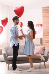 Photo of Happy young couple in living room decorated with heart shaped balloons. Valentine's day celebration