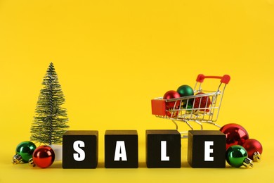 Photo of Word Sale made with black wooden cubes and Christmas decor on yellow background