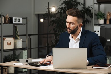 Man with calculator working on laptop at table in office, space for text