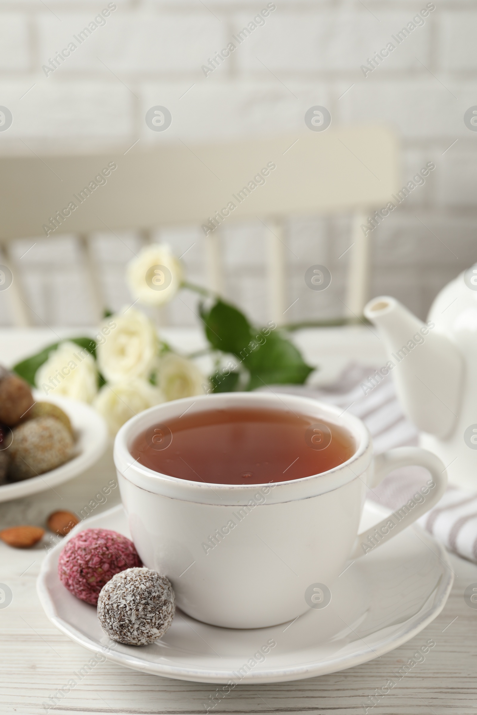 Photo of Cup of aromatic tea and delicious vegan candy balls on white wooden table, space for text
