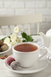 Cup of aromatic tea and delicious vegan candy balls on white wooden table, space for text