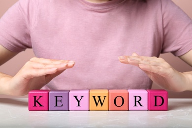 Photo of Woman demonstrating colorful cubes with word KEYWORD at grey marble table, closeup