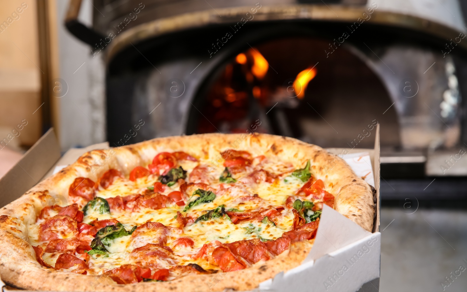 Photo of Delivery box with tasty Italian pizza near oven in restaurant, closeup