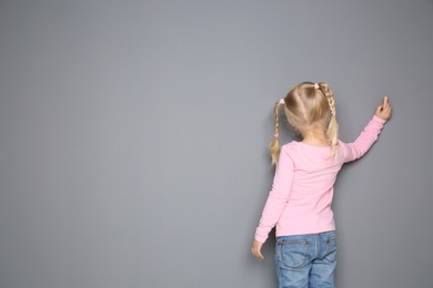 Little girl drawing with colorful chalk on gray background. Space for design