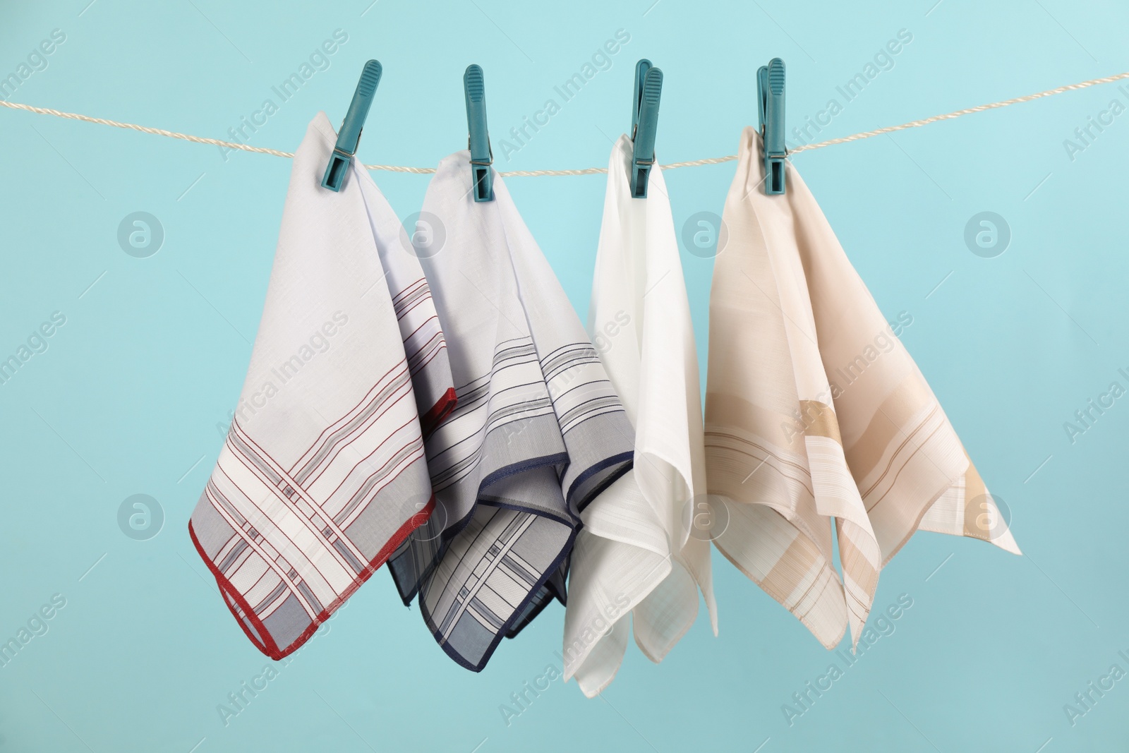 Photo of Many different handkerchiefs hanging on rope against light blue background