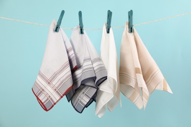 Photo of Many different handkerchiefs hanging on rope against light blue background