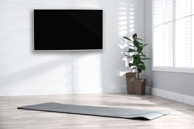 Image of Modern wide screen TV on white wall in room with yoga mat