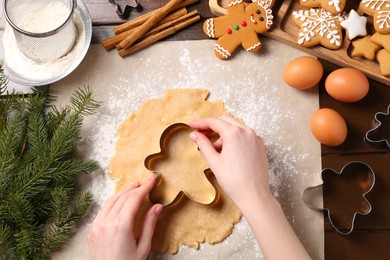 Photo of Woman making Christmas cookies with cutters at wooden table, top view