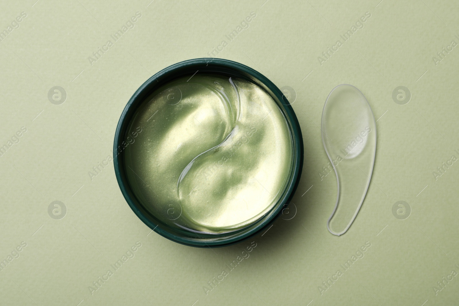 Photo of Under eye patches in jar and spatula on olive background, flat lay. Cosmetic product