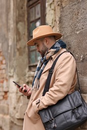 Photo of Handsome man in warm scarf with smartphone near wall outdoors