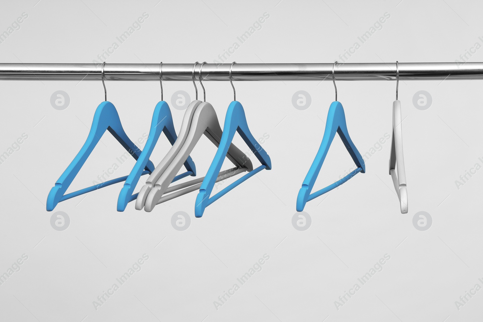 Photo of Empty clothes hangers on metal rail against light background