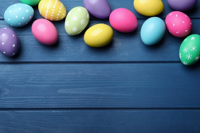 Colorful eggs on blue wooden background, flat lay with space for text. Happy Easter