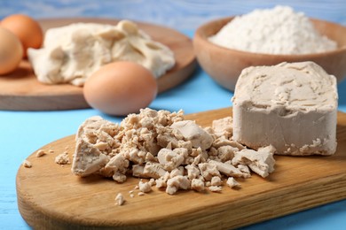 Photo of Pieces of compressed yeast, eggs and flour on light blue table, closeup