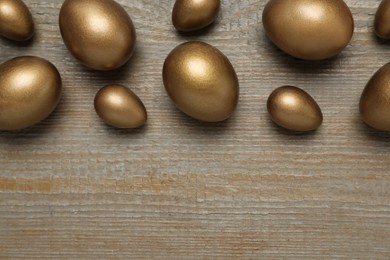 Golden eggs on wooden table, flat lay. Space for text
