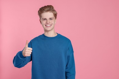 Photo of Teenage boy showing thumb up on pink background. Space for text