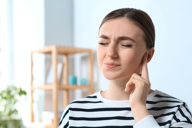 Young woman suffering from ear pain at home