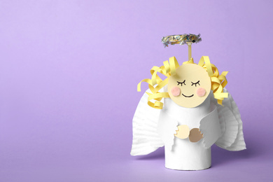 Toy angel made of toilet paper hub on lilac background. Space for text
