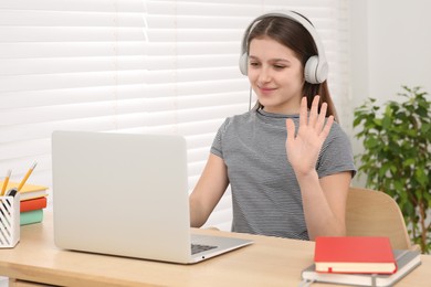 Cute girl using laptop and headphones at desk in room. Home workplace