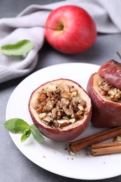 Photo of Tasty baked apples with nuts, honey, cinnamon sticks and mint on gray table, closeup