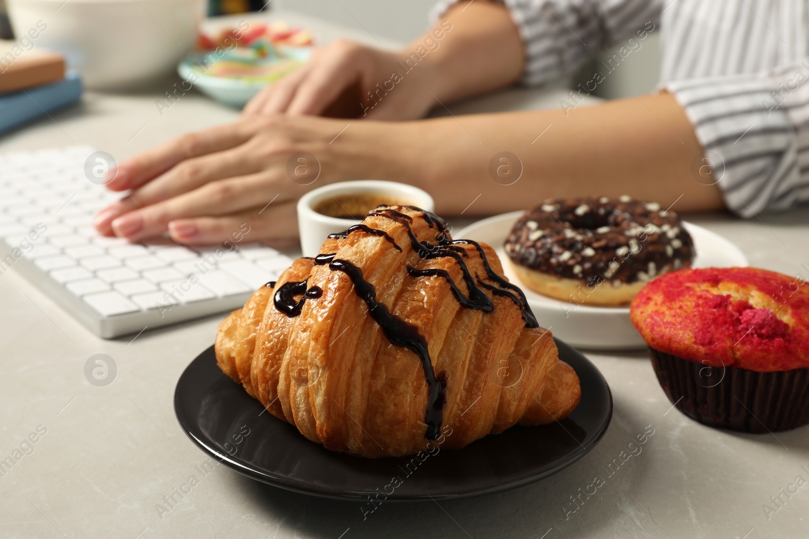 Photo of Bad eating habits. Woman working on computer at light grey marble table with different snacks, selective focus