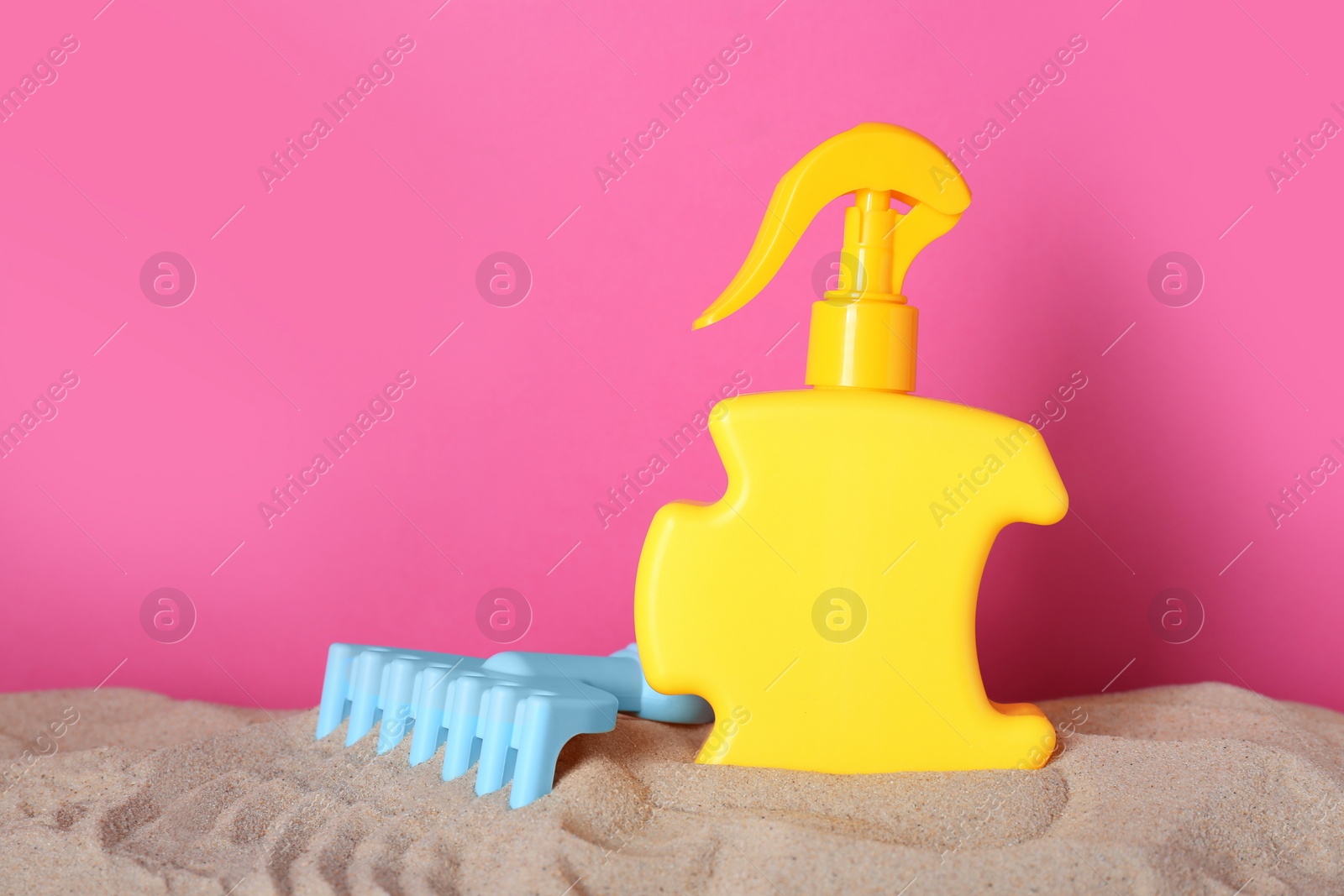 Photo of Suntan product and plastic beach toy on sand against pink background