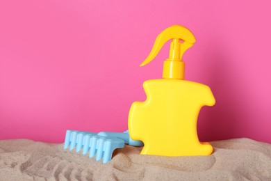 Suntan product and plastic beach toy on sand against pink background